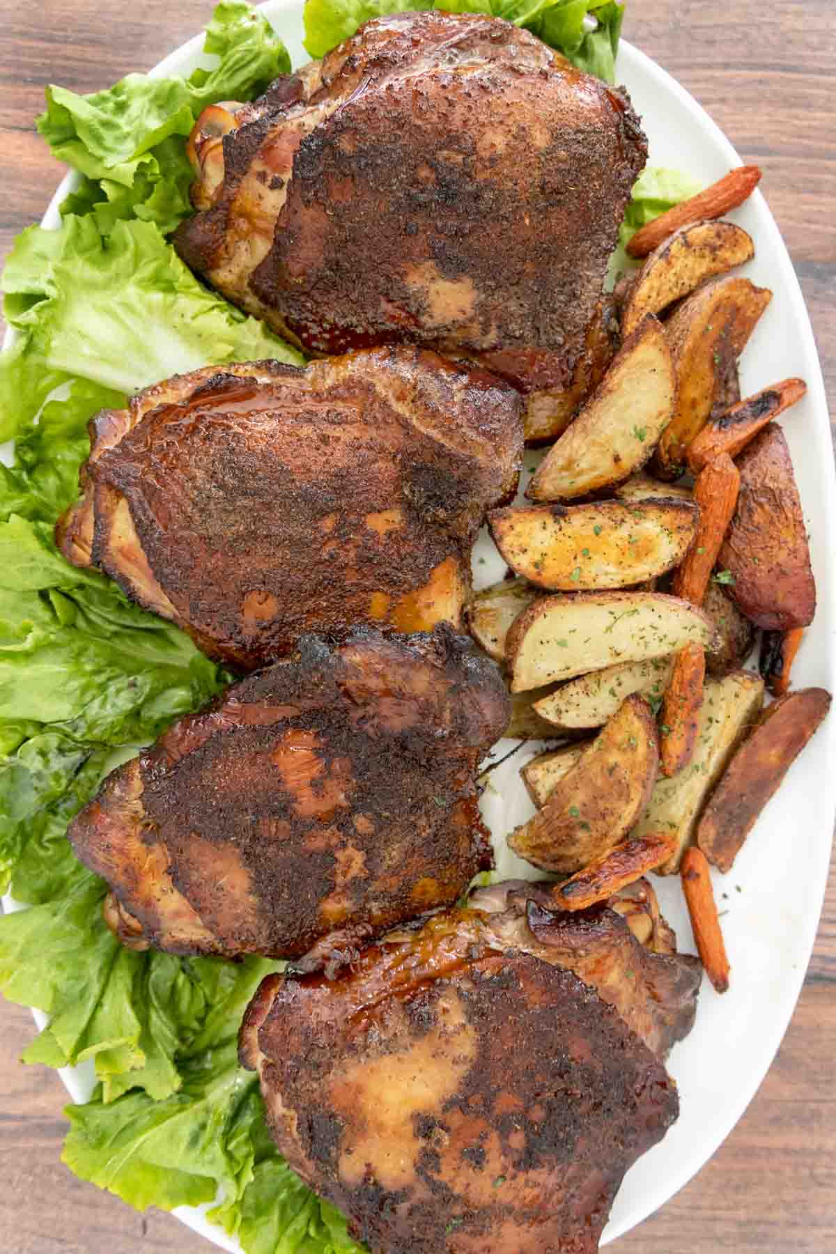 Smoked turkey thighs on a bed of romaine leaves on a white platter with crispy potato wedges.