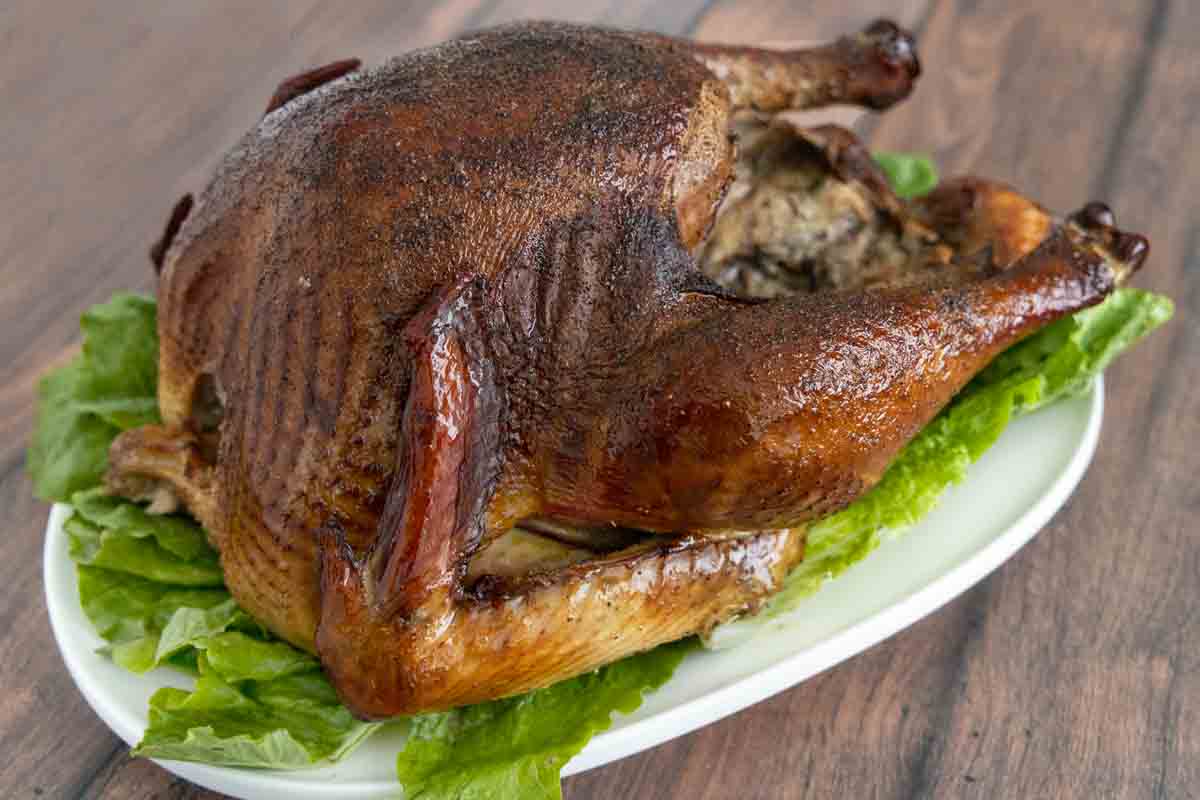 whole smoked turkey on a white platter with greens.