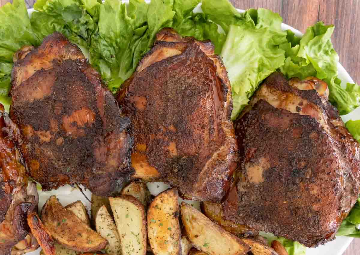 Smoked turkey thighs on a bed of romaine leaves on a white platter with crispy potato wedges.