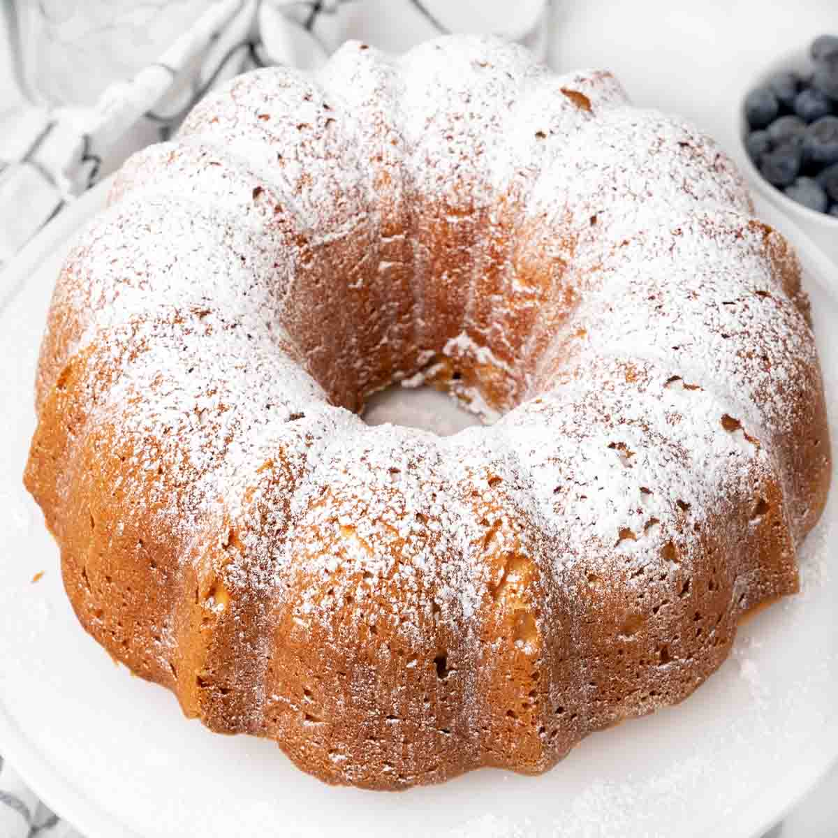 Whole cream cheese pound cake dusted with powdered sugar on white platter.