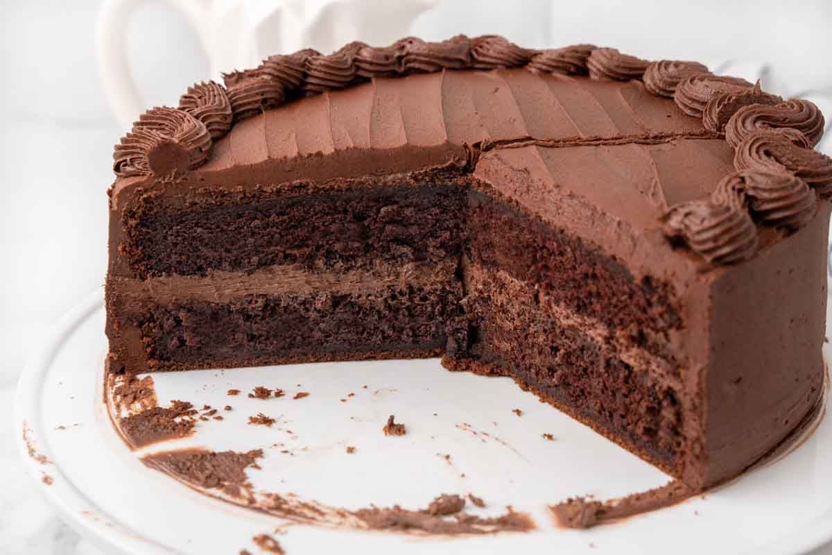 view of whole devil's food cake on cake plate with slices taken out of the cake.