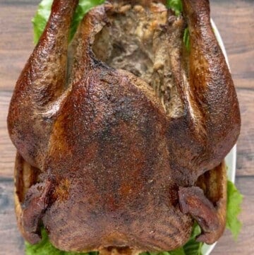 whole smoked turkey on a white platter with greens.