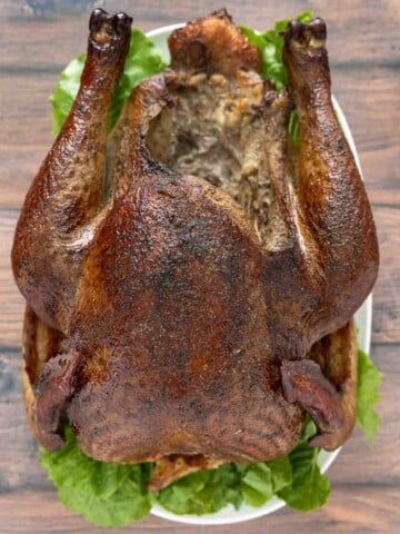 whole smoked turkey on a white platter with greens.