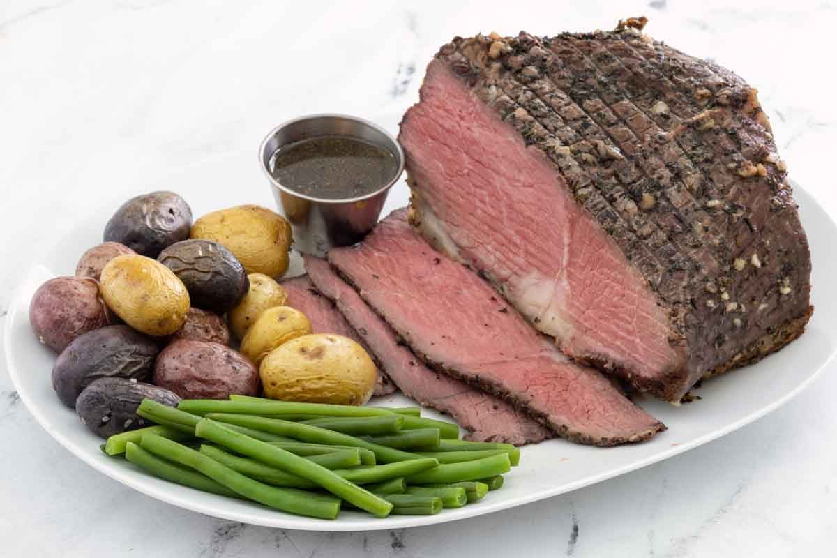 Sliced bottom round roast with potatoes and green beans on a white platter.