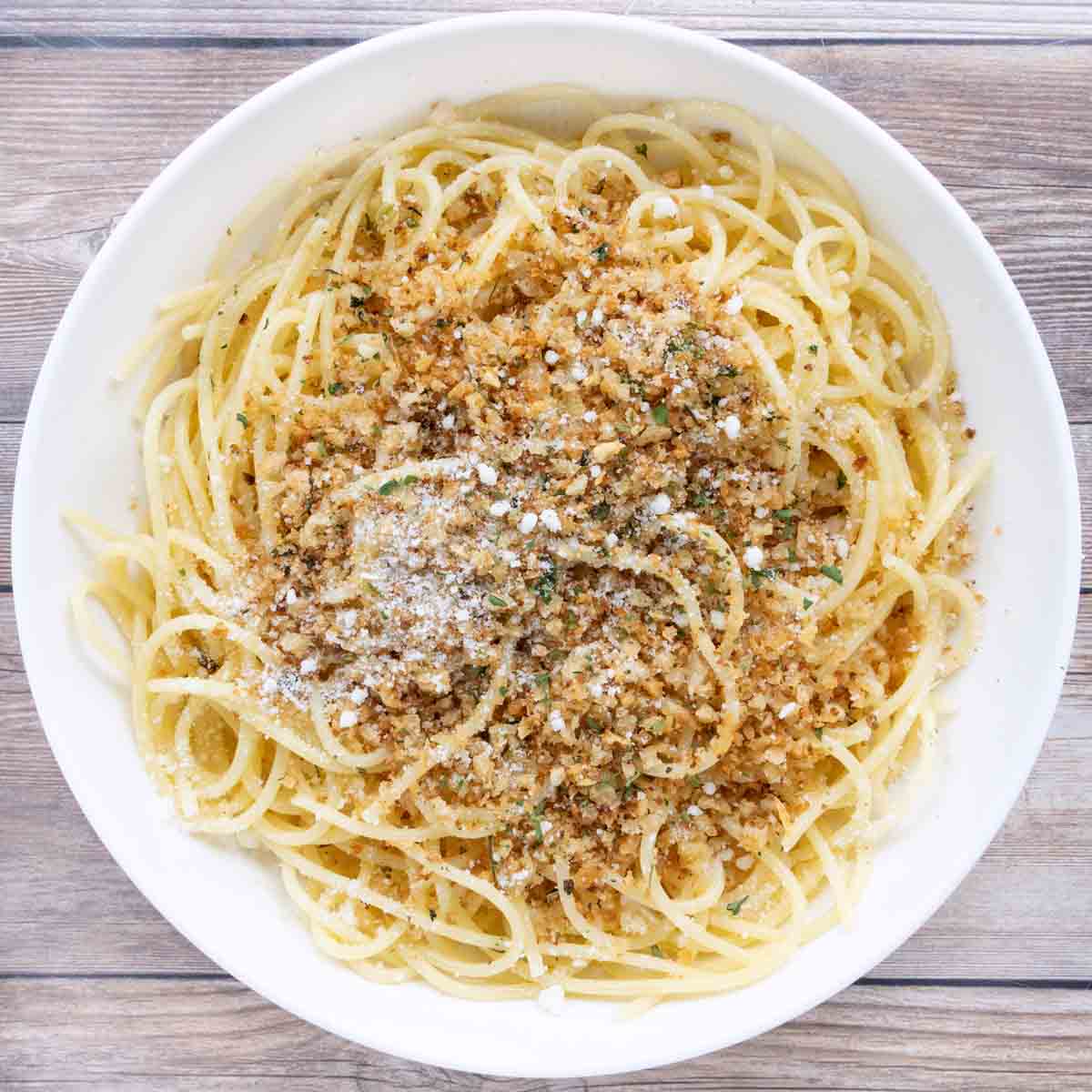 Spaghetti with pangrattato and grated cheese in a white bowl.