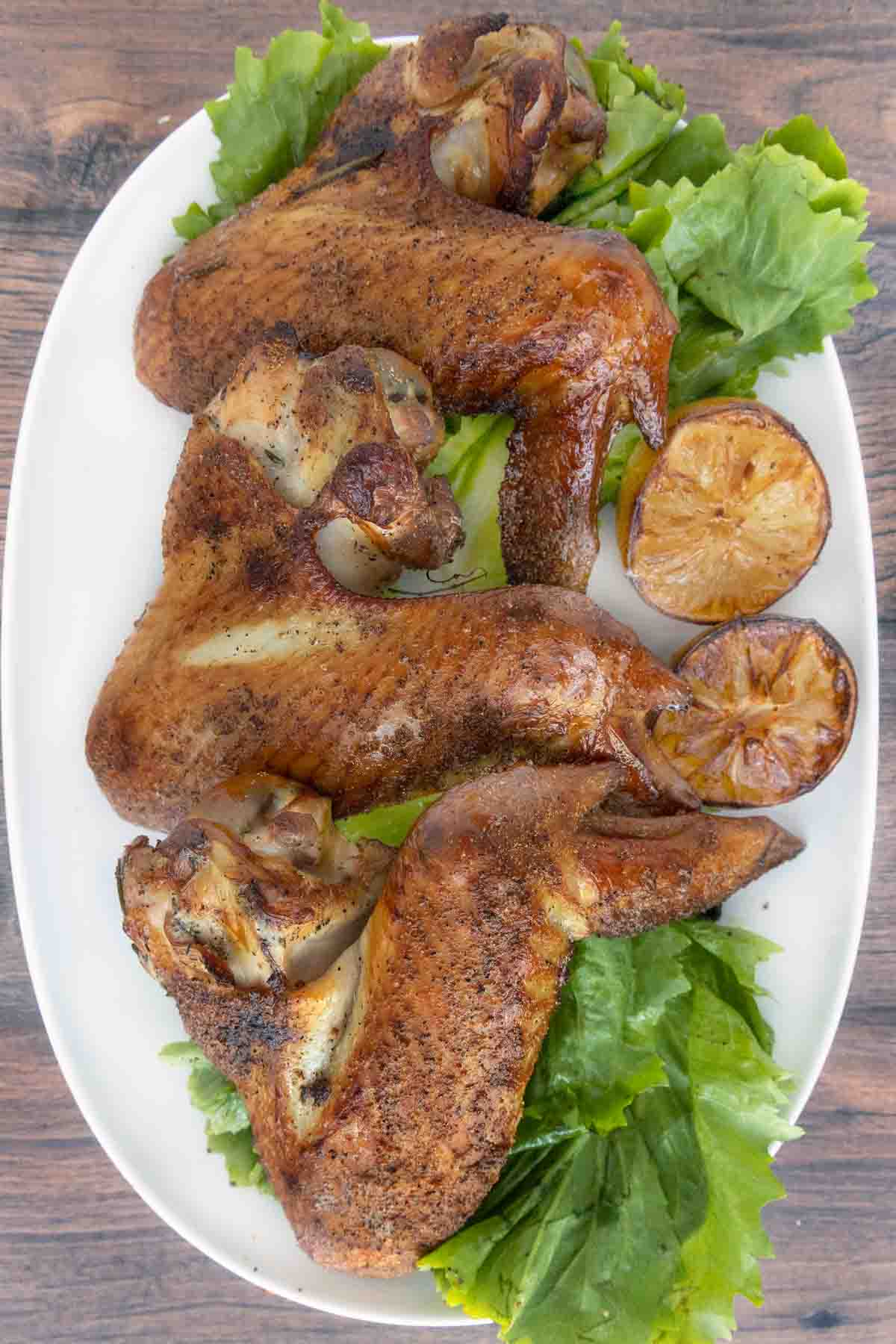 Smoked turkey wings on a white plate with greens.
