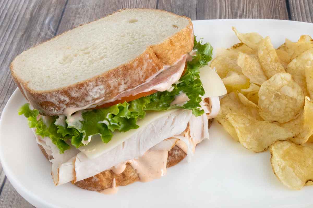 Turkey and cheese sandwich with lettuce and sriracha mayo on a white plate.