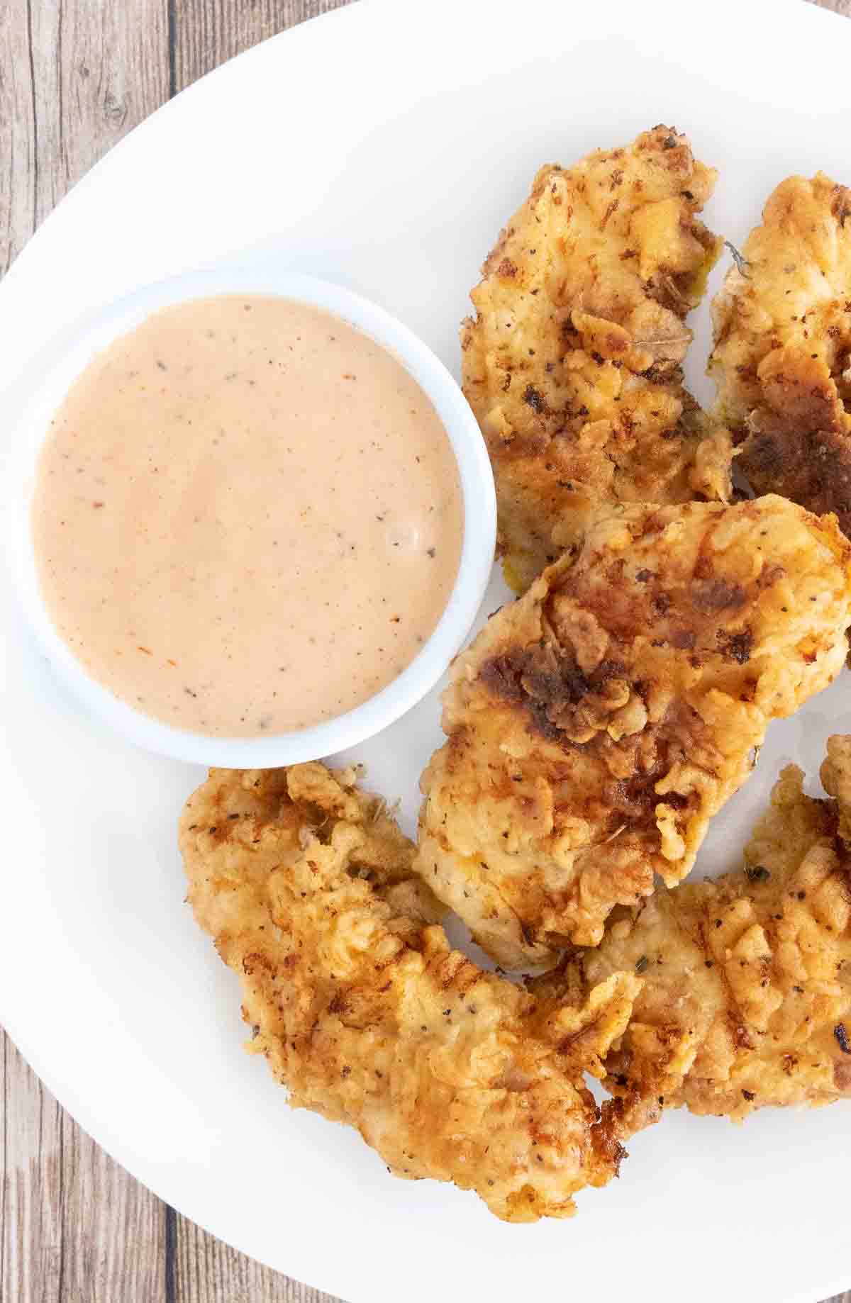 Chicken dipping sauce with chicken tenders on a white plate.