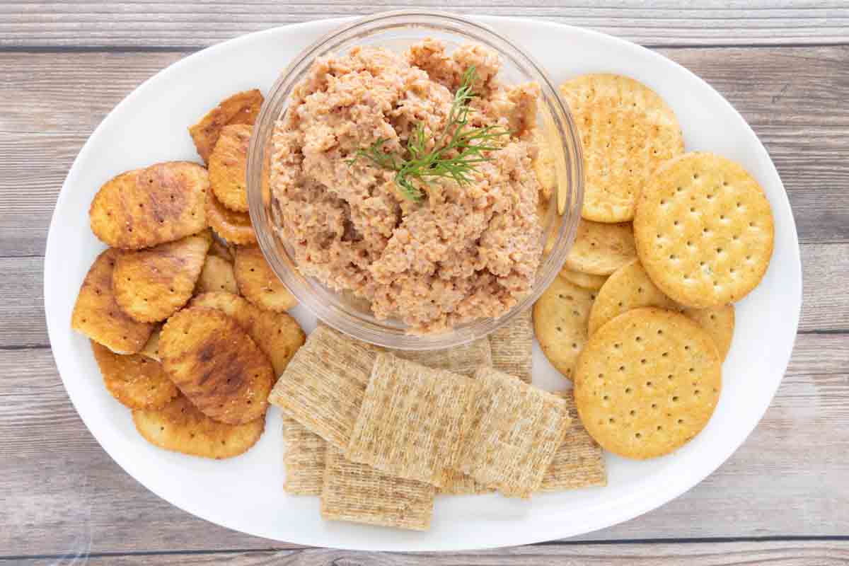 Deviled ham in a glass bowl on a white platter with assorted crackers.