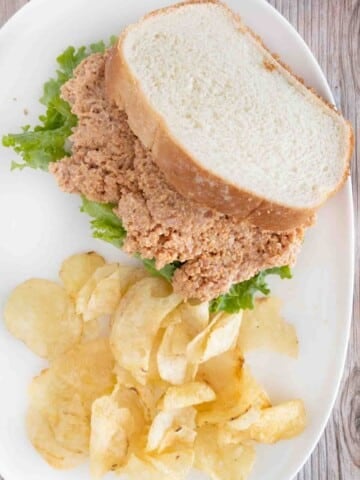 Deviled ham sandwich with potato chips on a white plate.