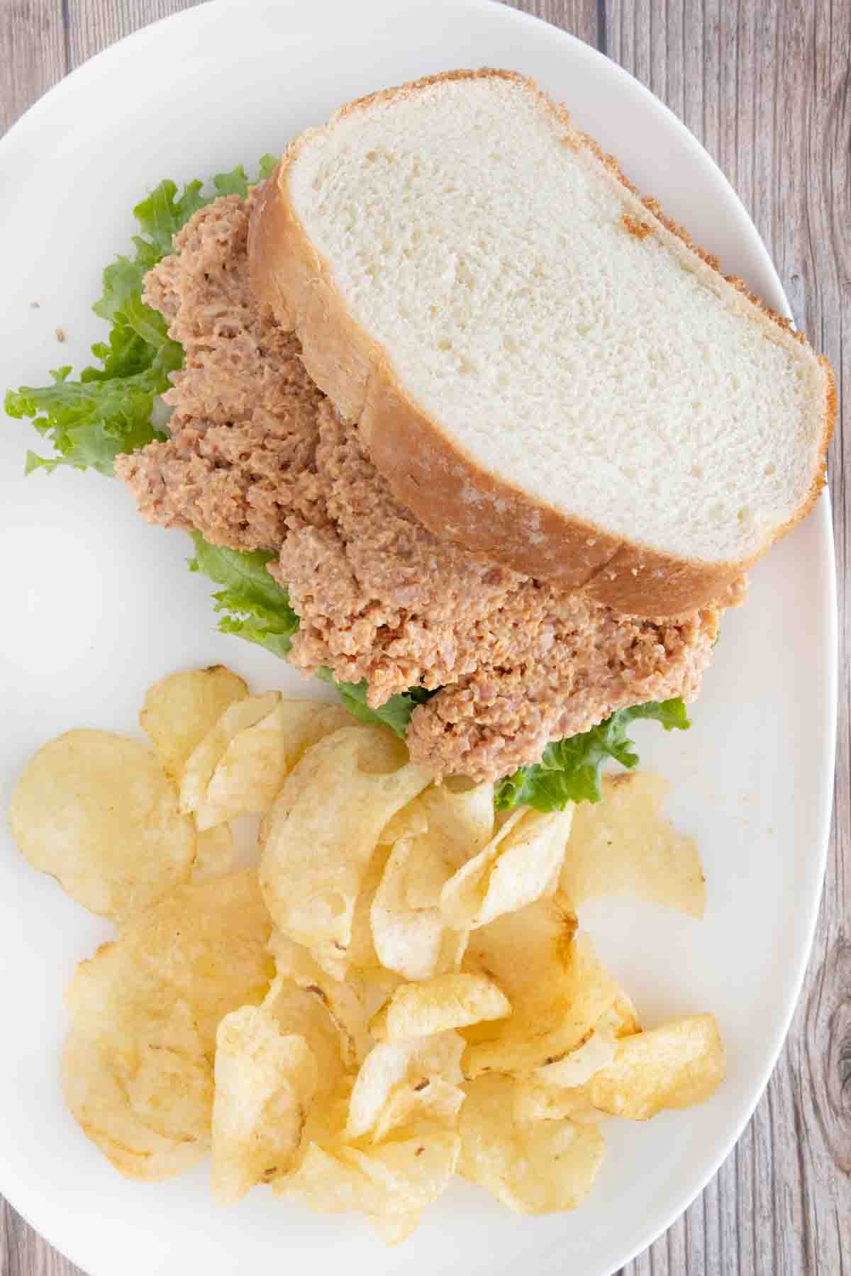 Deviled ham sandwich with potato chips on a white plate.