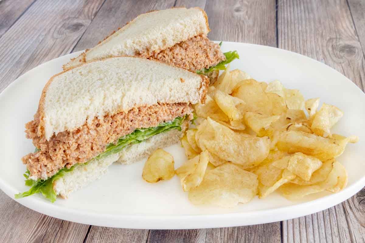 Deviled ham sandwich with potato chips on a white plate.