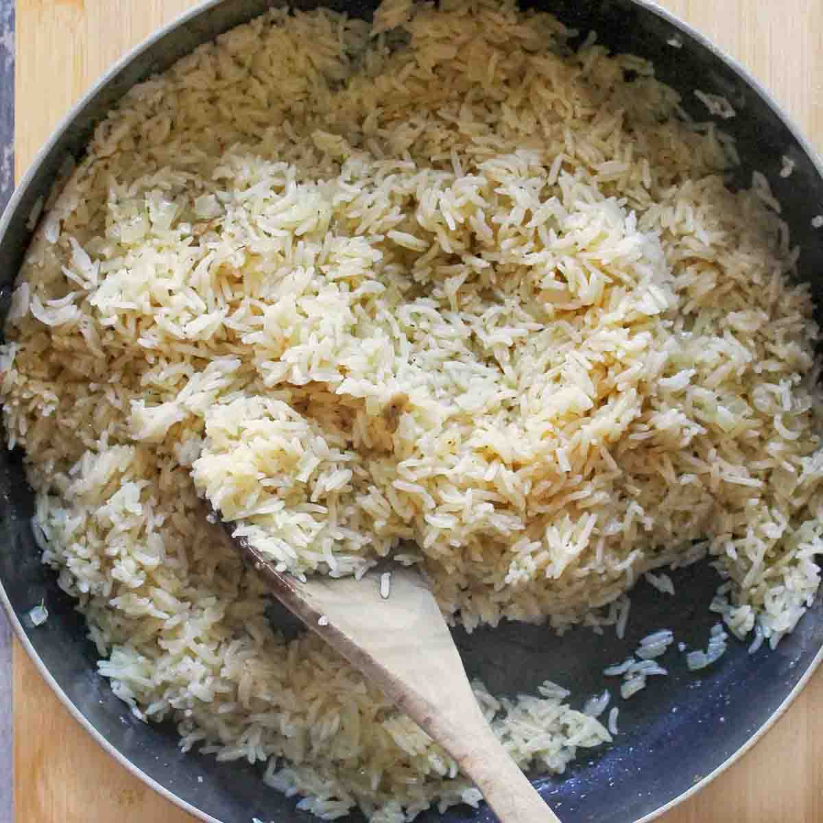 Wooden spoon fluffing rice in pot.