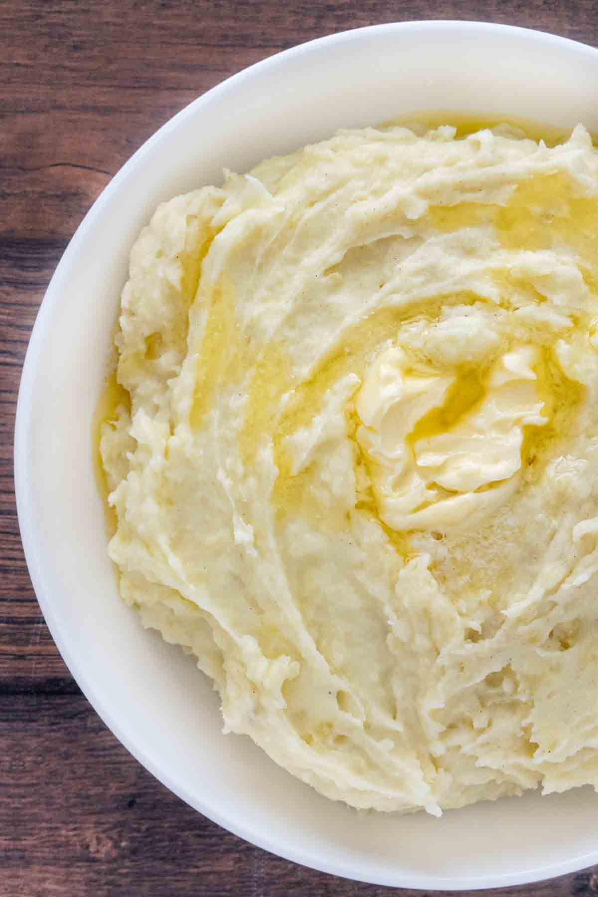 Mashed potatoes with butter melting on top in white bowl.