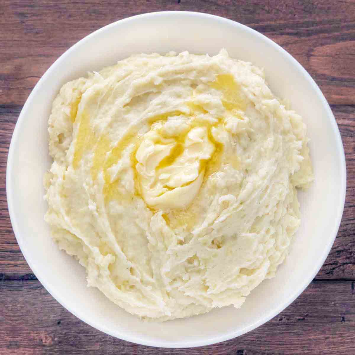 Mashed potatoes with butter melting on top in white bowl.