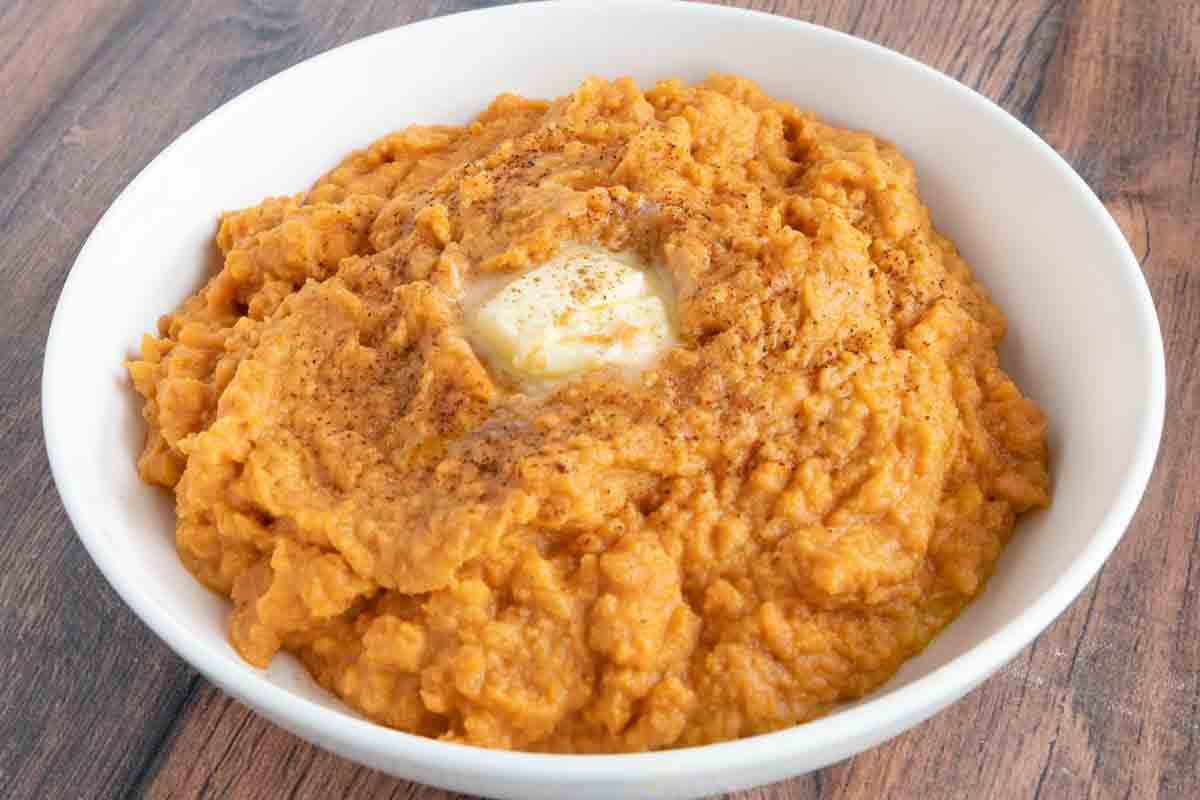 Mashed sweet potatoes with a pat of butter in a white bowl.