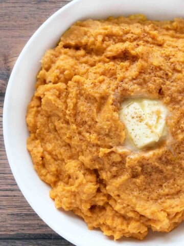 Mashed sweet potatoes with a pat of butter in a white bowl.