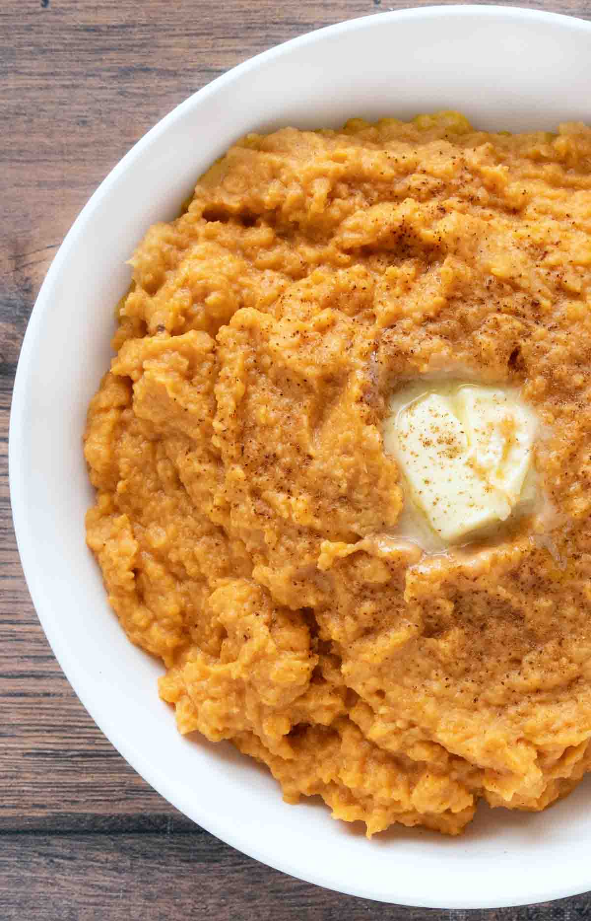 Mashed sweet potatoes with a pat of butter in a white bowl.