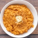 Mashed sweet potatoes with a pat of butter in a white bowl