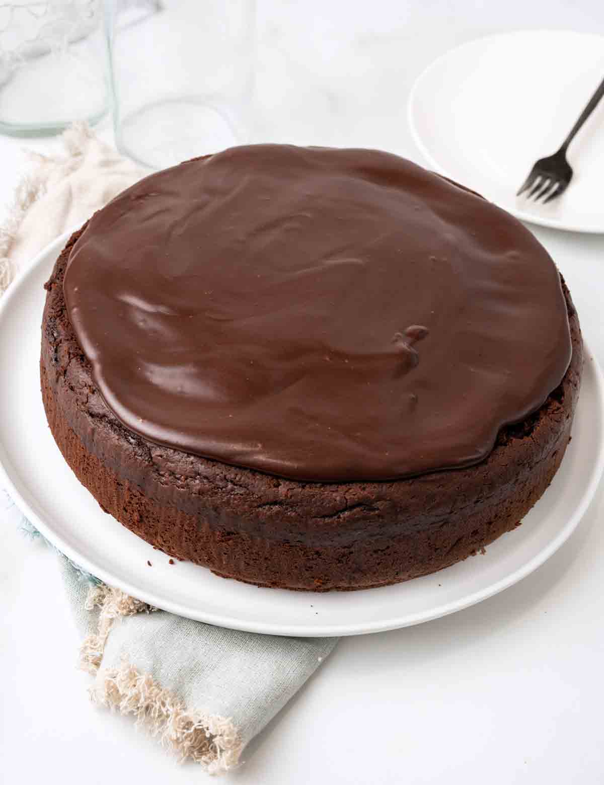 Whole chocolate mud cake on white platter.
