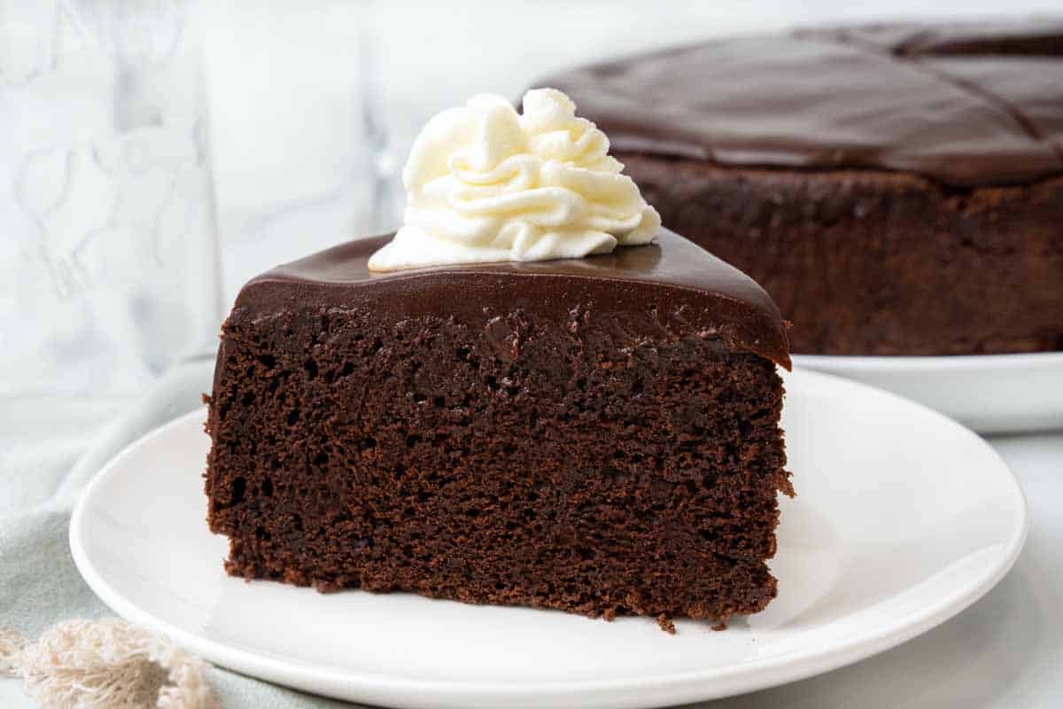 Slice of chocolate mud cake with whipped cream on a white plate.