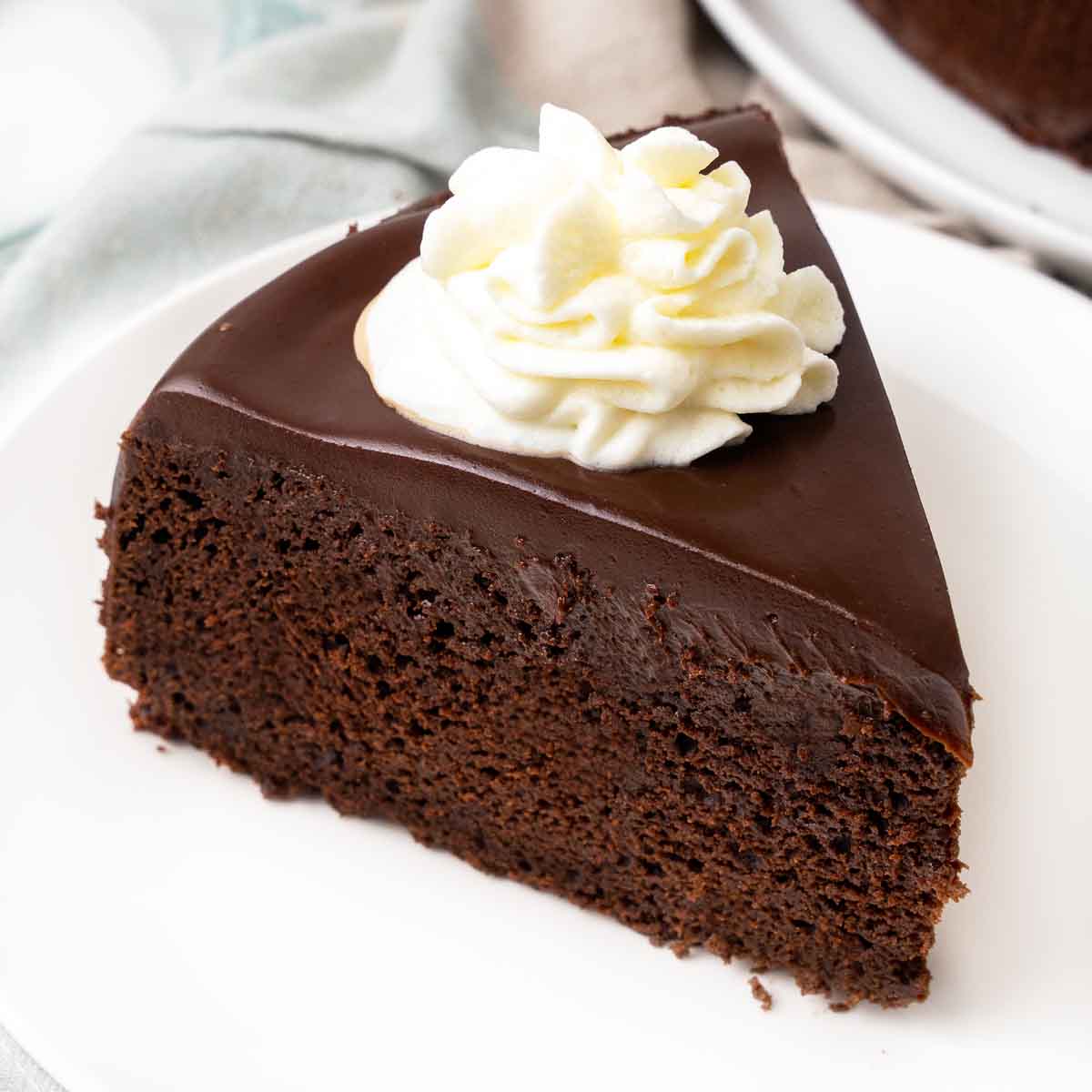 Slice of chocolate mud cake with whipped cream on a white plate.