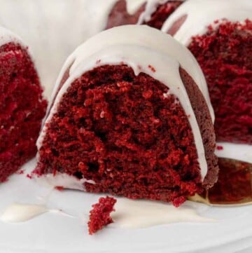 Slice of red velvet cake on a white platter with remainder of cake.