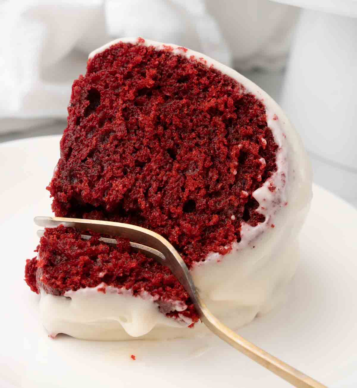 Slice of red velvet cake on a white plate with a fork taking a piece out.