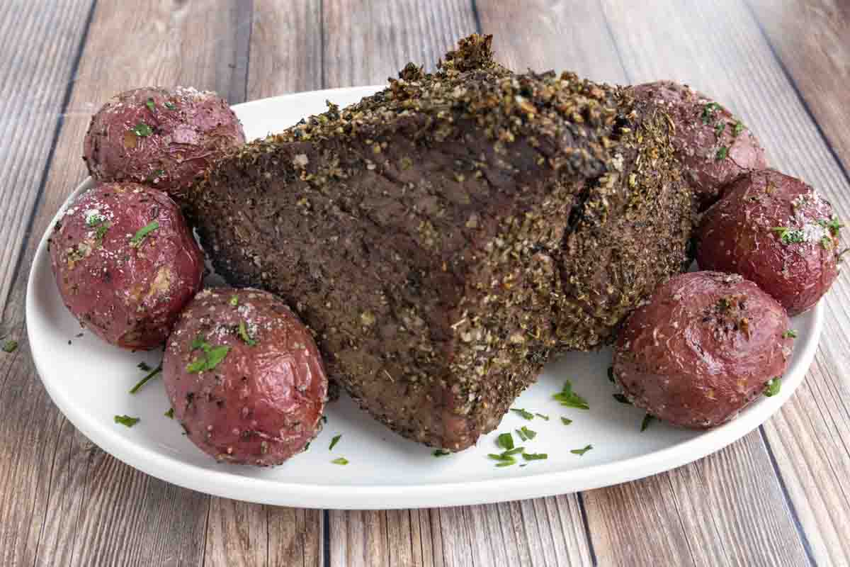 Cooked top round roast with potatoes on a white platter.