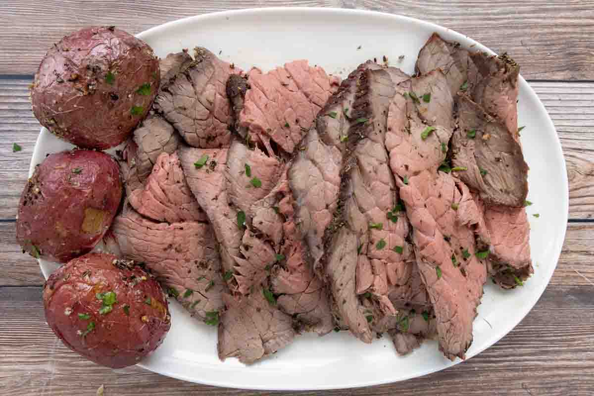 sliced top round roast with potatoes on a white platter.