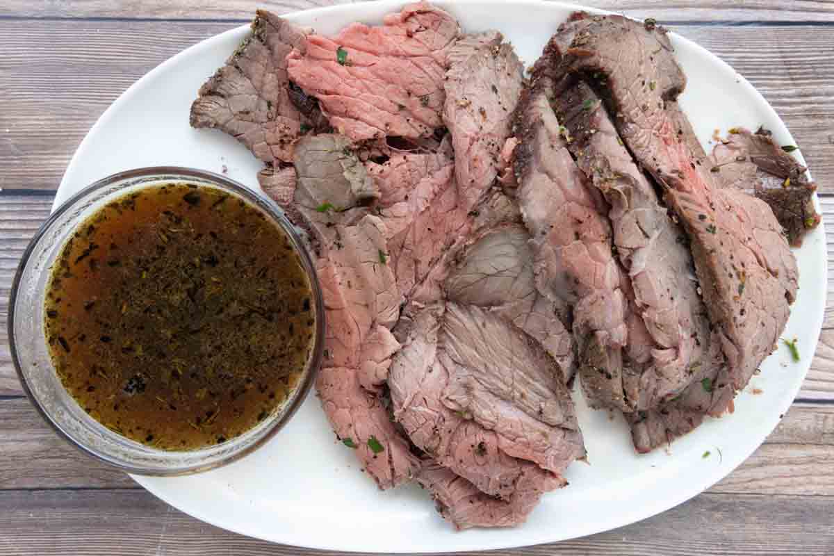 sliced top round roast with au jus on a white platter.
