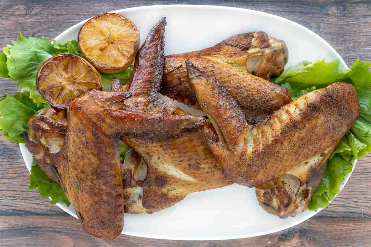 Smoked turkey wings on a white plate with greens.