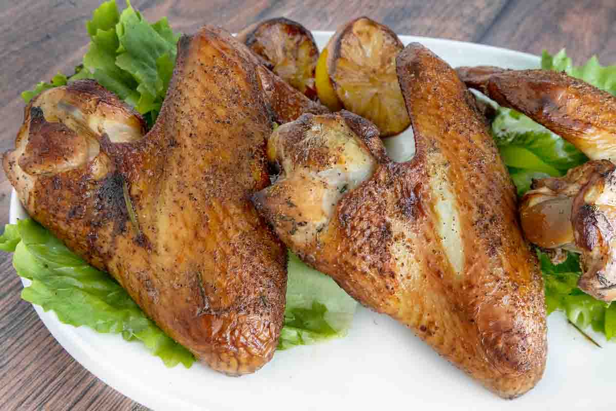 Smoked turkey wings on a white plate with greens.