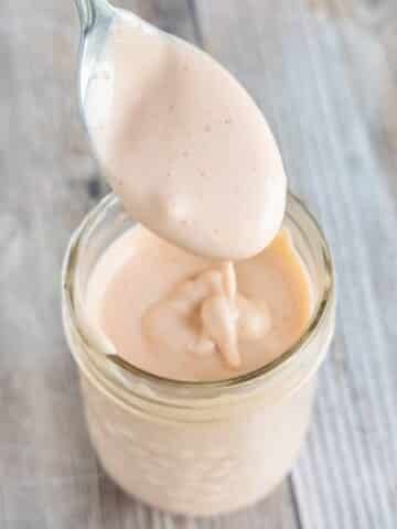 Sriracha mayo in a glass jar with a spoon coming out of it.