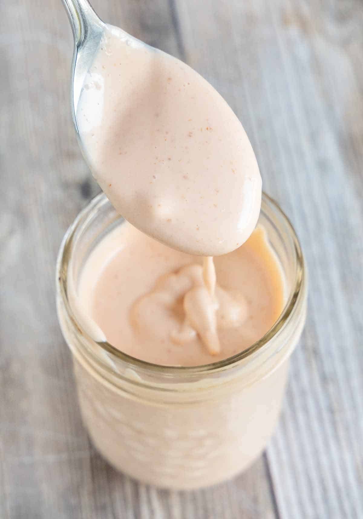 Sriracha mayo in a glass jar with a spoon coming out of it.