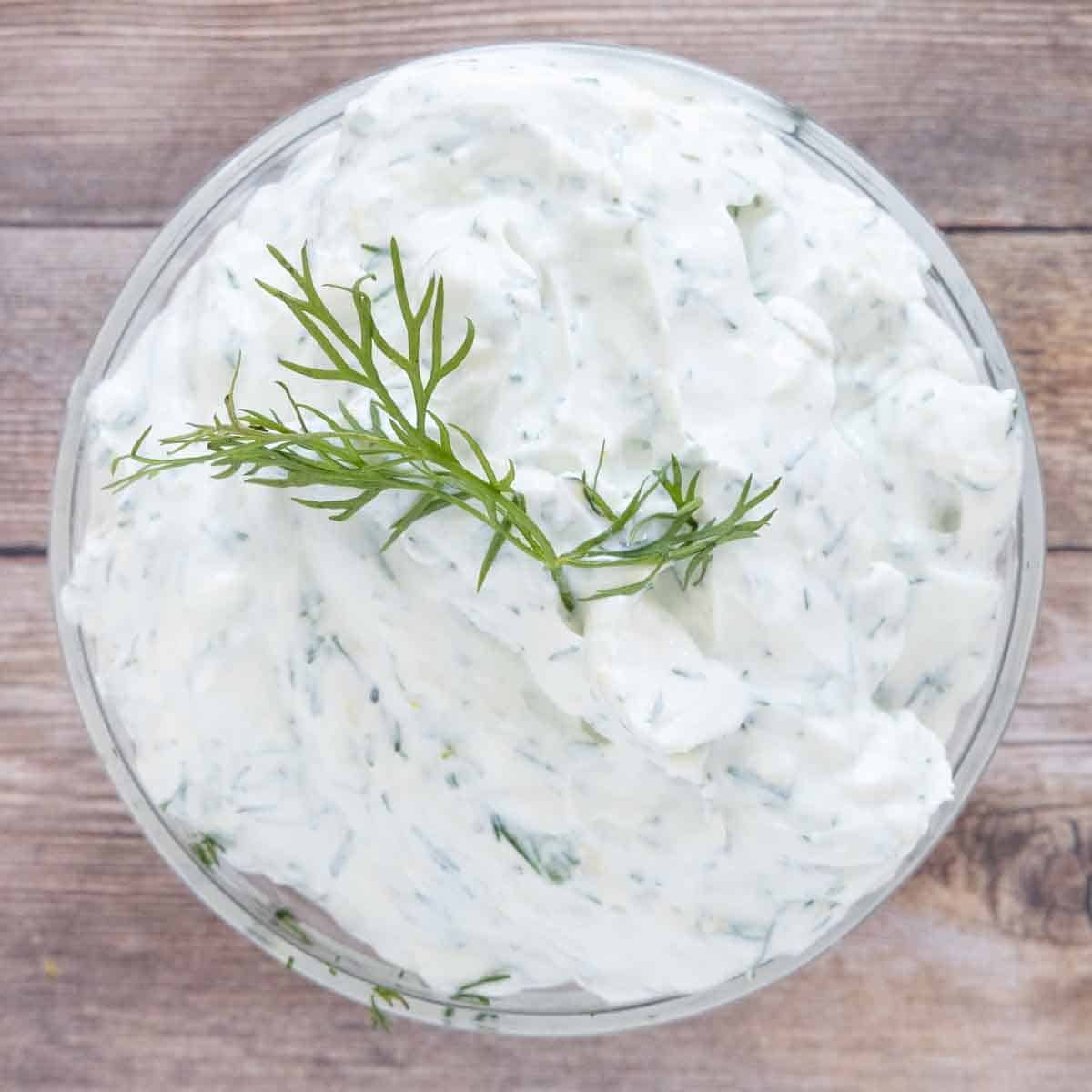 Dill yogurt sauce with a sprig of dill  on top in a glass bowl.