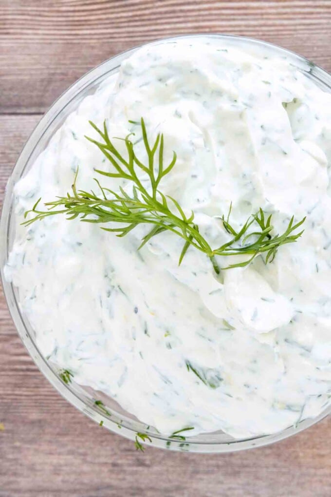 Yogurt dill dip with a sprig of dill on top in a glass bowl.