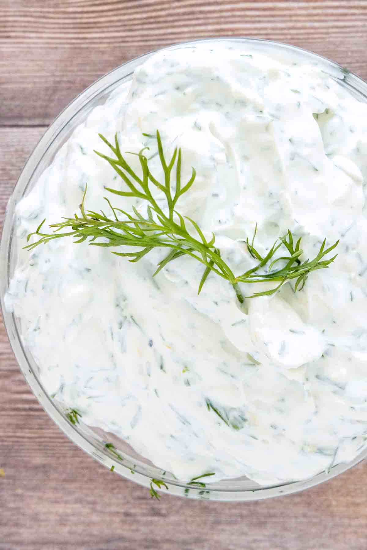 Dill yogurt sauce with a sprig of dill  on top in a glass bowl.