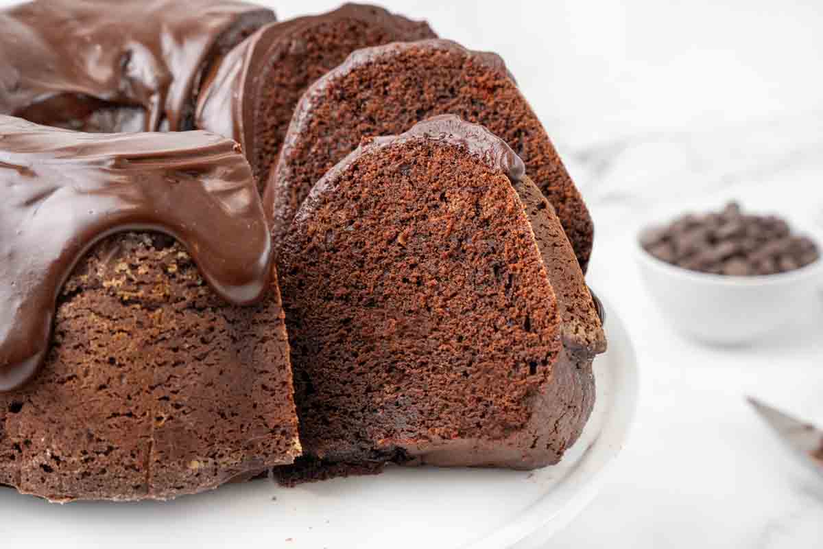 slices of chocolate brownie cake stacked by whole cake on white platter.