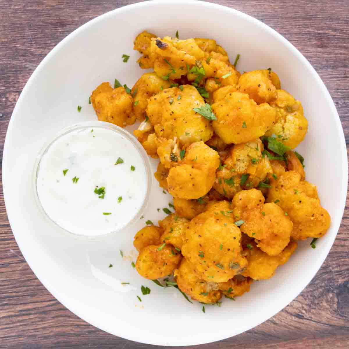 Deep fried cauliflower bites in a white bowl with ranch dressing.