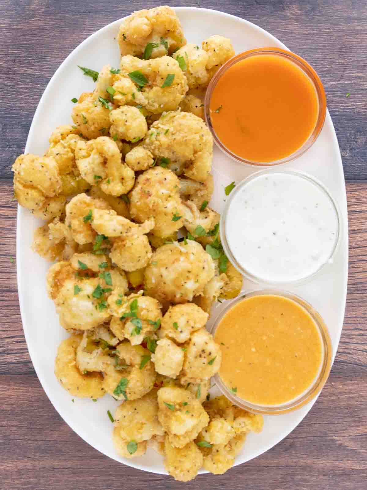 Deep fried cauliflower bites on a white platter with three dipping sauces.