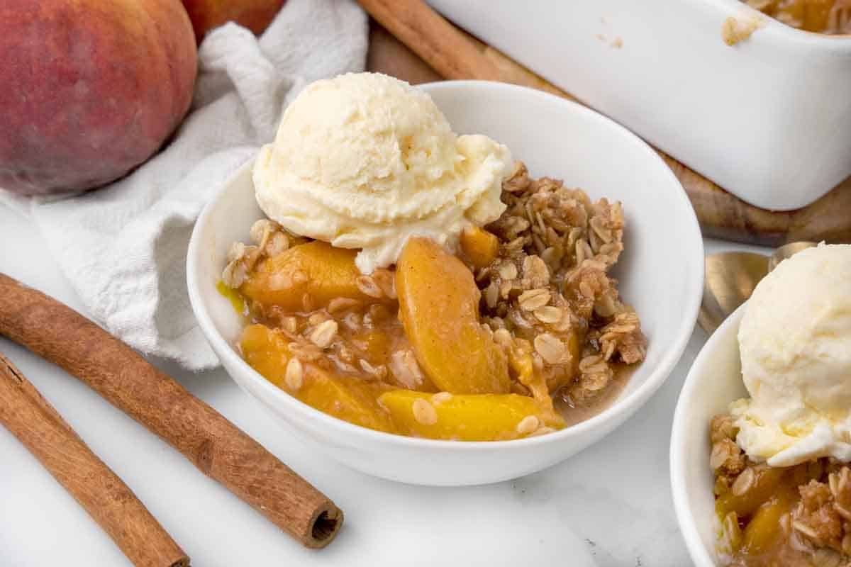 Peach Crisp topped with vanilla ice cream in a white bowl.