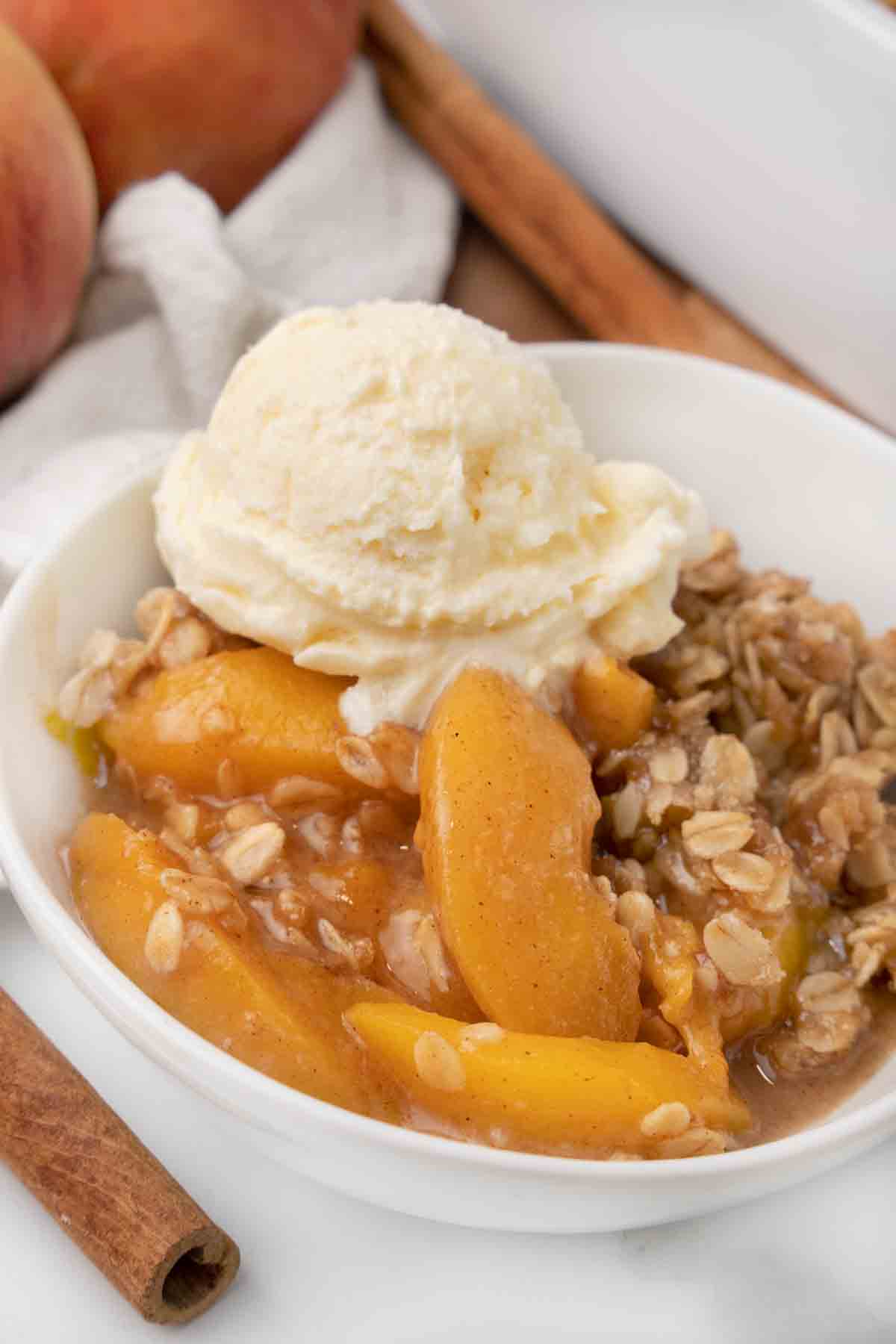Peach Crisp topped with vanilla ice cream in a white bowl.