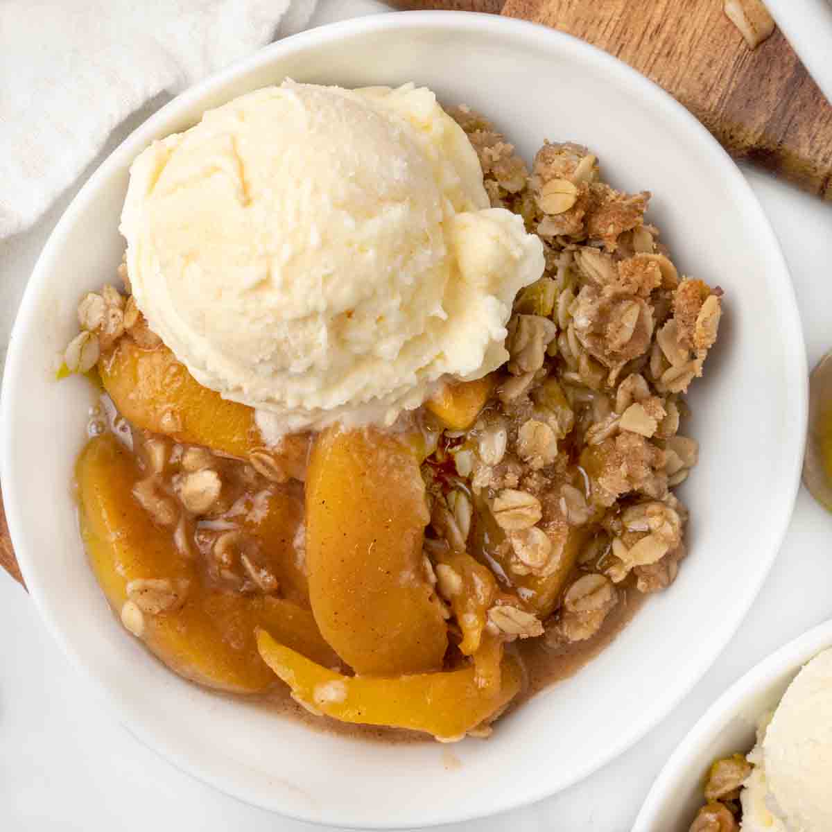 Peach Crisp topped with vanilla ice cream in a white bowl.