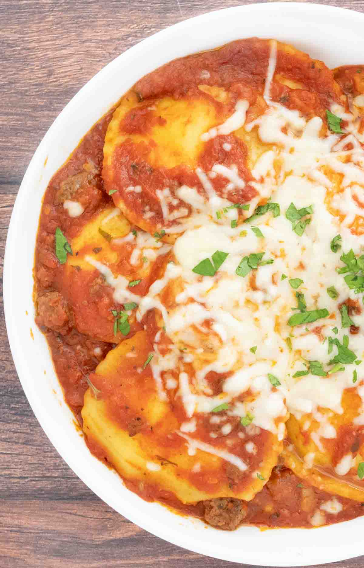 Baked Ravioli with sprinkle of chopped parsley in white bowl.