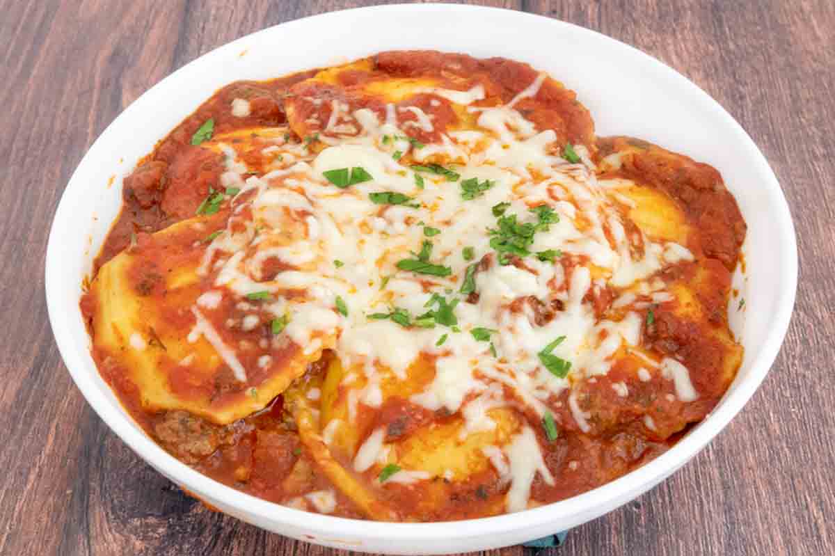 Baked Ravioli with sprinkle of chopped parsley in white bowl.