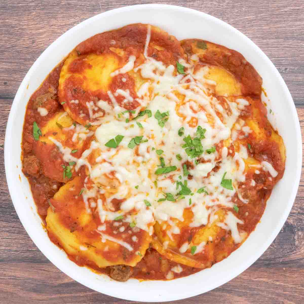 Baked Ravioli with sprinkle of chopped parsley in white bowl.