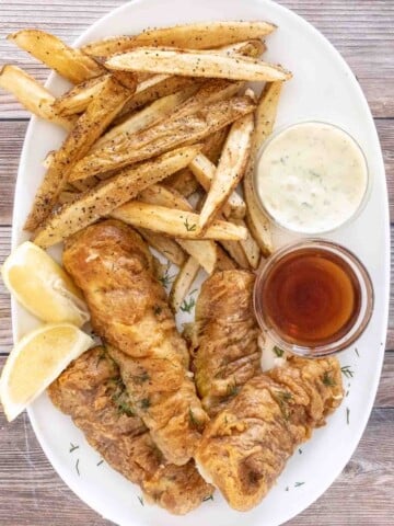 Fish and chips on a white platter with malt vinegar and tarter sauce.