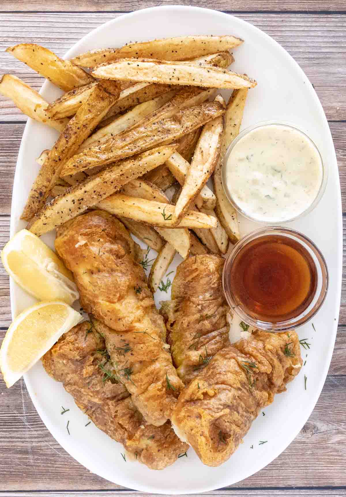 Fish and chips on a white platter with malt vinegar and tarter sauce.