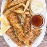 Fish and chips on a white platter with malt vinegar and tarter sauce.